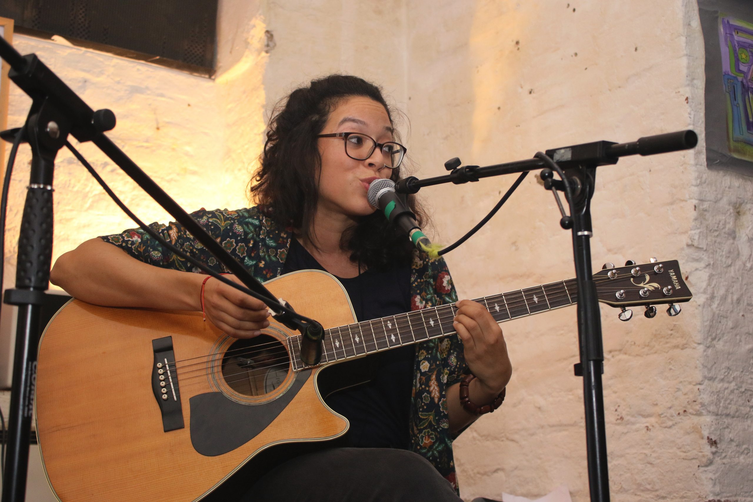 Junge Frau mit Brille, MIkrofon spielt Gitarre und schaut nach links